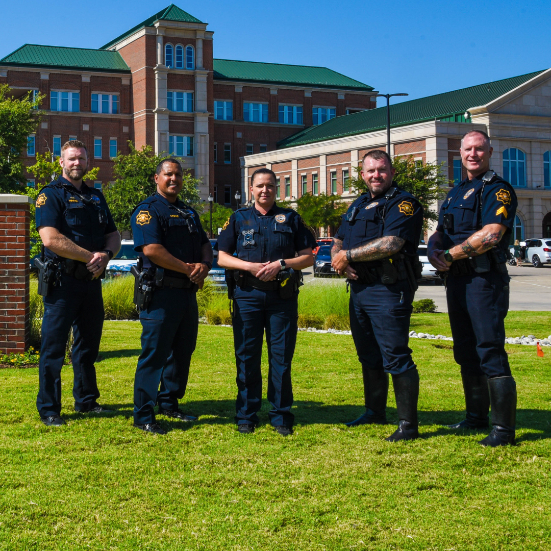 Four male and one female Grapevine Police officers stand outside police building