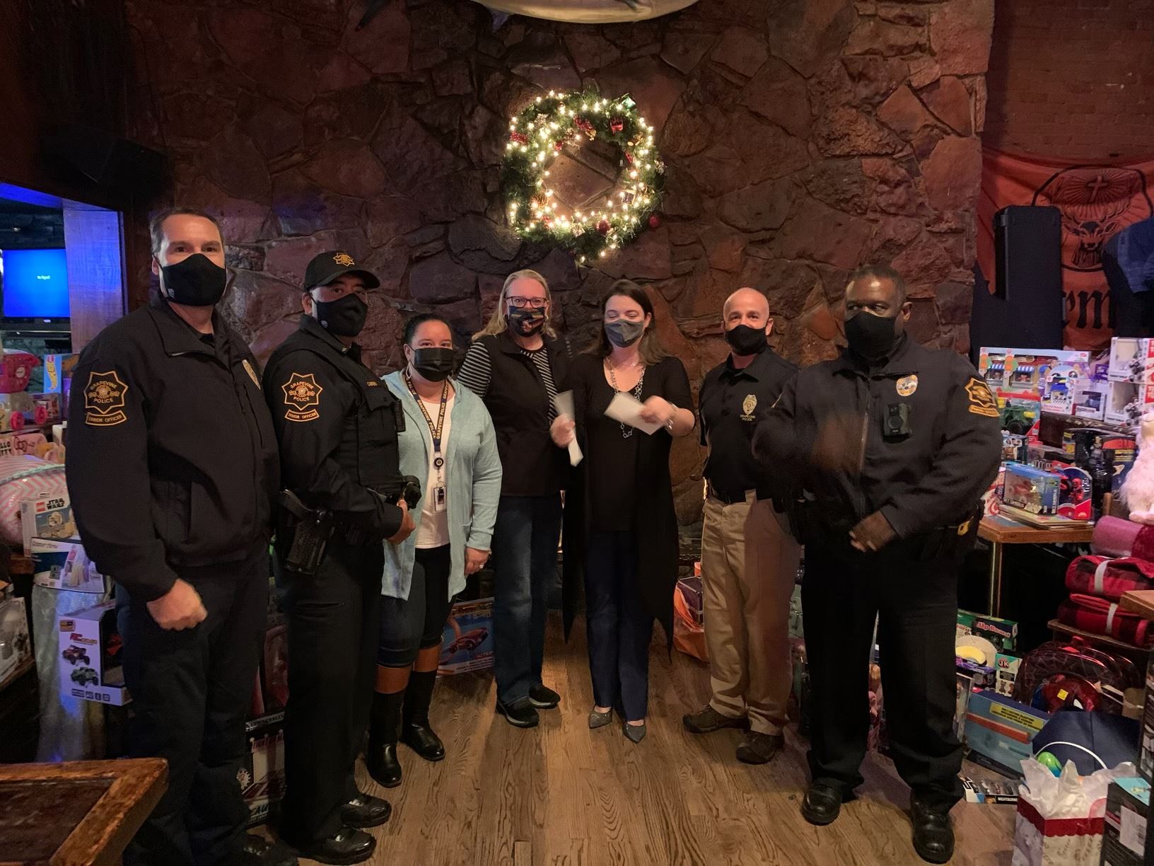 group of masked adults and police officers holding check for Santa Cops